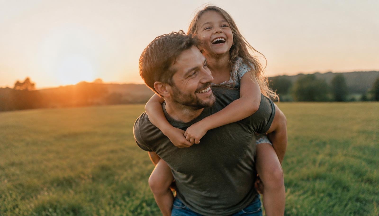 A father giving his laughing daughter a piggyback ride at sunset
